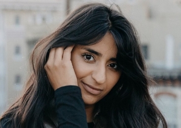 UX Design graduate Sana Maqsood outside with hand behind ear, in long dark hair. Photo.