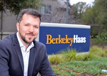 Thiago Santos Medeiros poses and smiles next to the Haas school of business sign on campus.