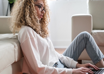 woman sitting on floor and leaning on couch using laptop