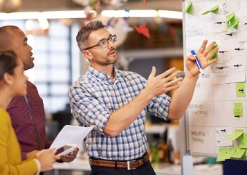 Man pointing at whiteboard with sticky notes while 2 colleagues look on