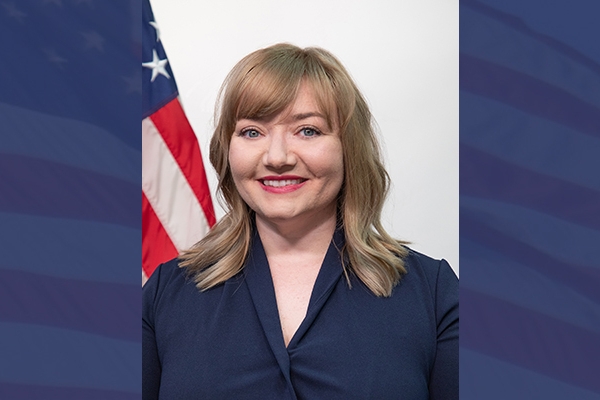 Headshot of Lacy Kelly Ramos in front of U.S. flag on blue background