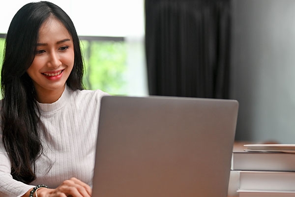 Stock image of a female Asian writer writing on laptop with books on table