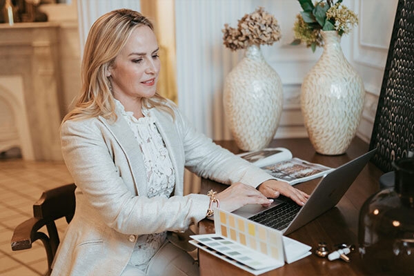 Certificate Program in Interior Design graduate Amber Lowi on laptop at desk with color palette