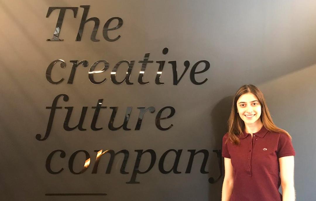 Maria poses in front of a sign at her job at the FutureBrand company